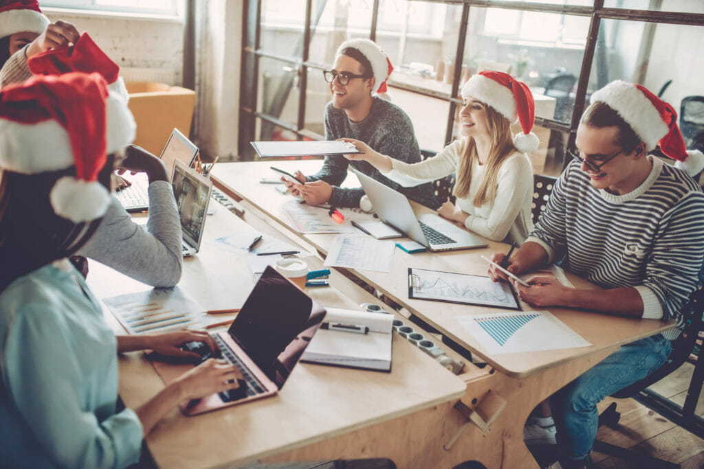 Group of young business people working on holiday emails in Santa hats.